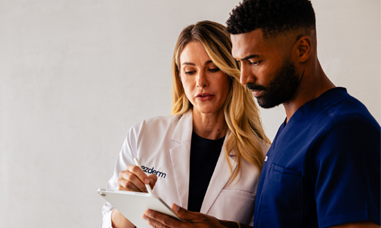 A dermatologist is showing a patient chart on an iPad to her medical assistant.