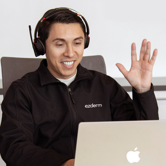 An Ezderm support representative wearing a headset is in front of his laptop and waving to the screen.
