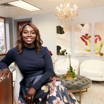 Photo of Dr. Mercy Odueyungbo, MD, sitting on a chair in the waiting room of her dermatology practice, Lilly Dermatology